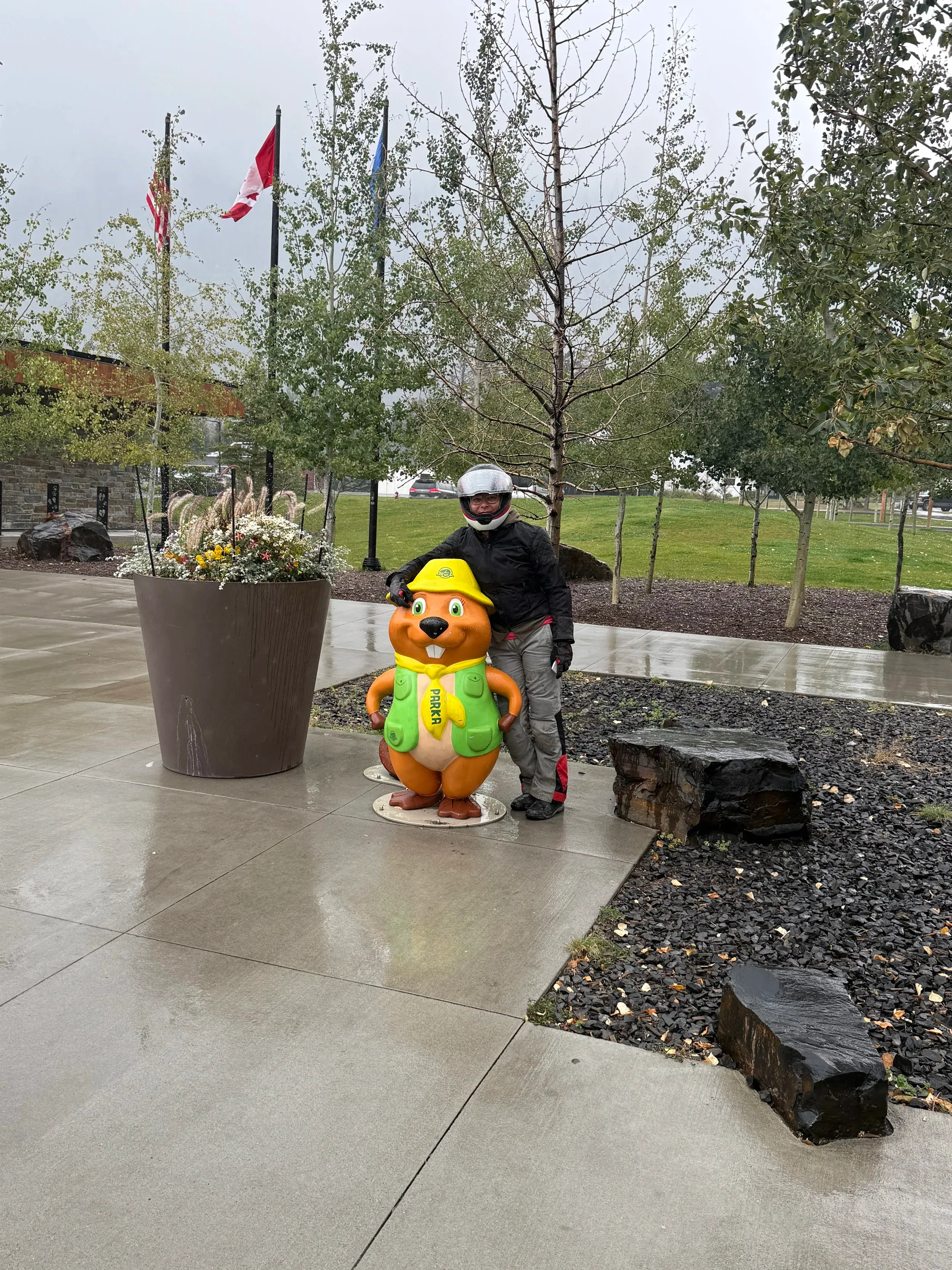 Person in motorcycle gear standing next to a park ranger statue on a rainy day