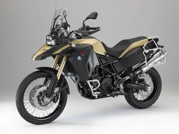 Yellow and black BMW adventure motorcycle with a windshield, side mirrors, and luggage rack in a studio setting.